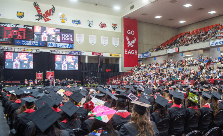 Commencement photo taken behind the rows of grads in caps and gowns looking at the speaker.