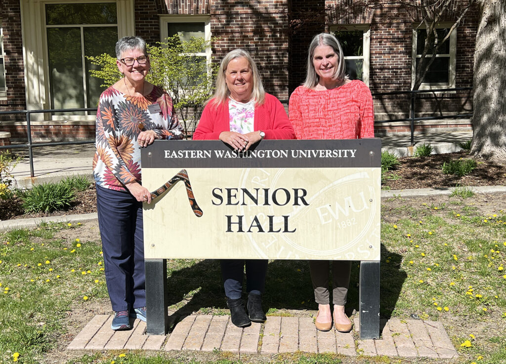 Cyndy Stevenson and two social work faculty standing by the Senior Hall sign. One is holding a boomerang.