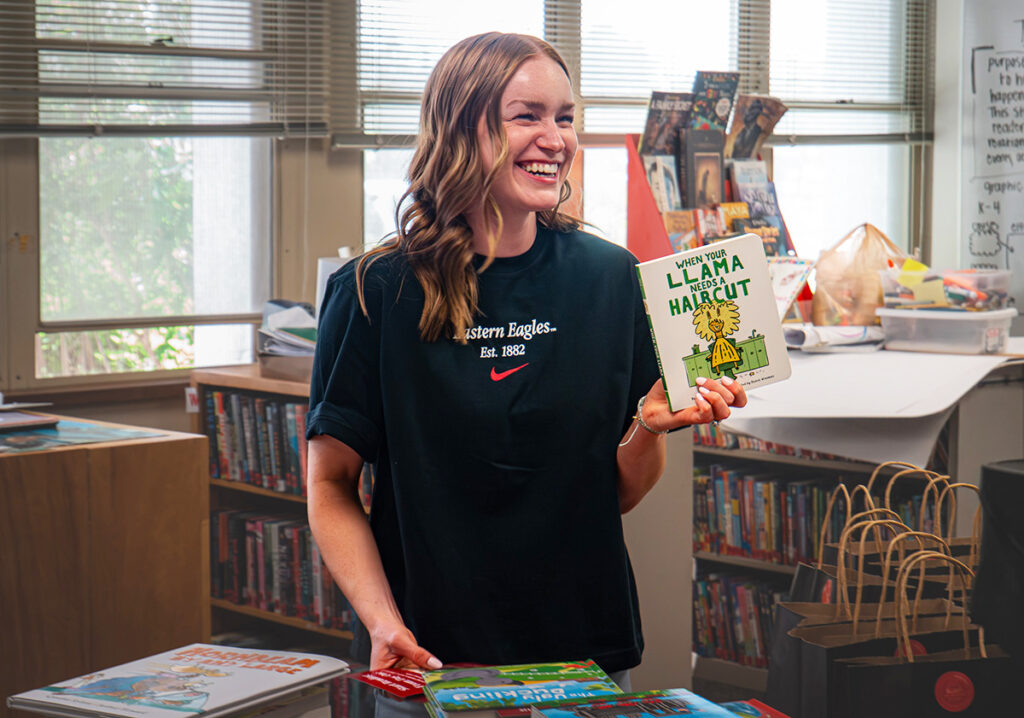 Smiling student holds up a book about a lama needing a haricut.