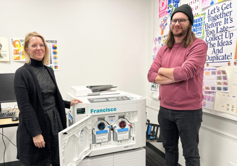 Two design faculty stand near a Risograph, in winter 2024, that was added to the 4D Lab.
