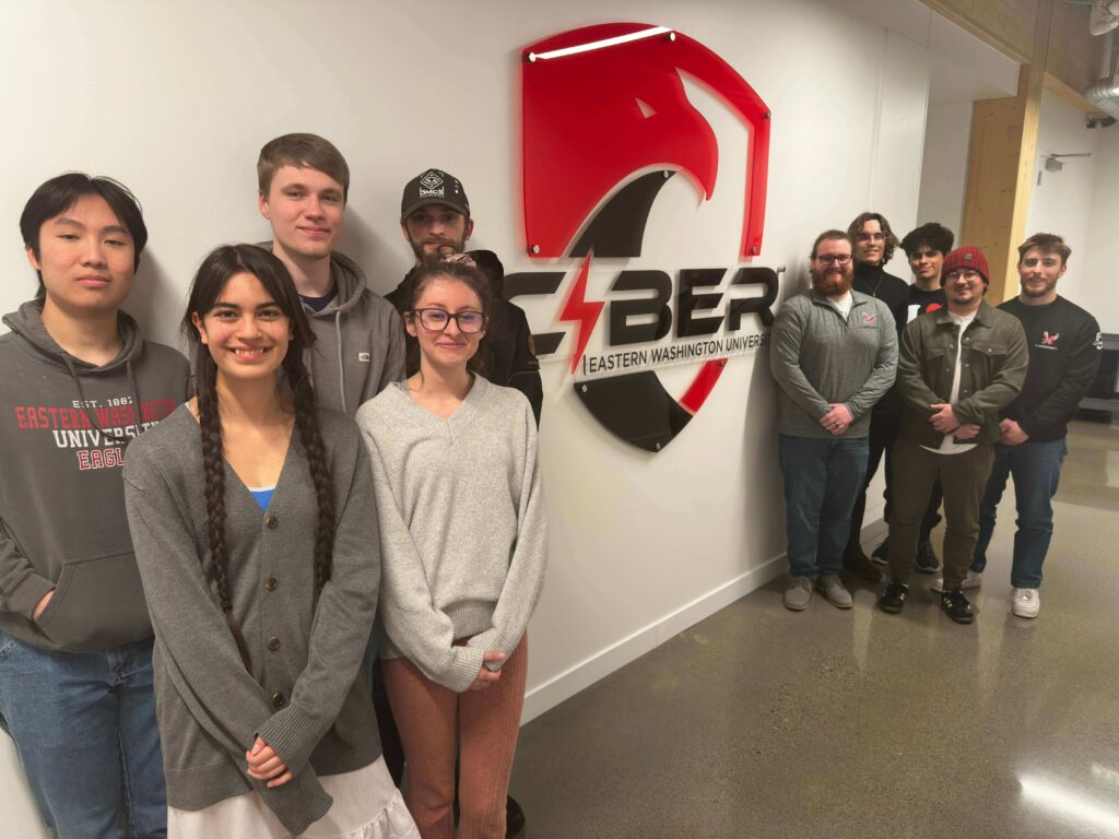 Nine students pose with cybersecurity sign.