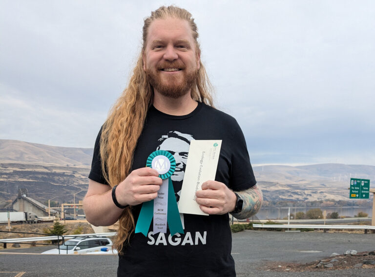 Jeff Schell pictured outside holding his award ribbon and envelope.